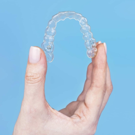 Woman holding invisible transparent aligner invisalign or plastic orthodontic braces, clear-plastic retainer on blue background