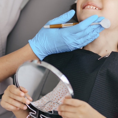 Cute little girl sitting on a modern dental chair and having dental consultation with dentist