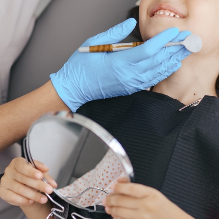 Cute little girl sitting on a modern dental chair and having dental consultation with dentist