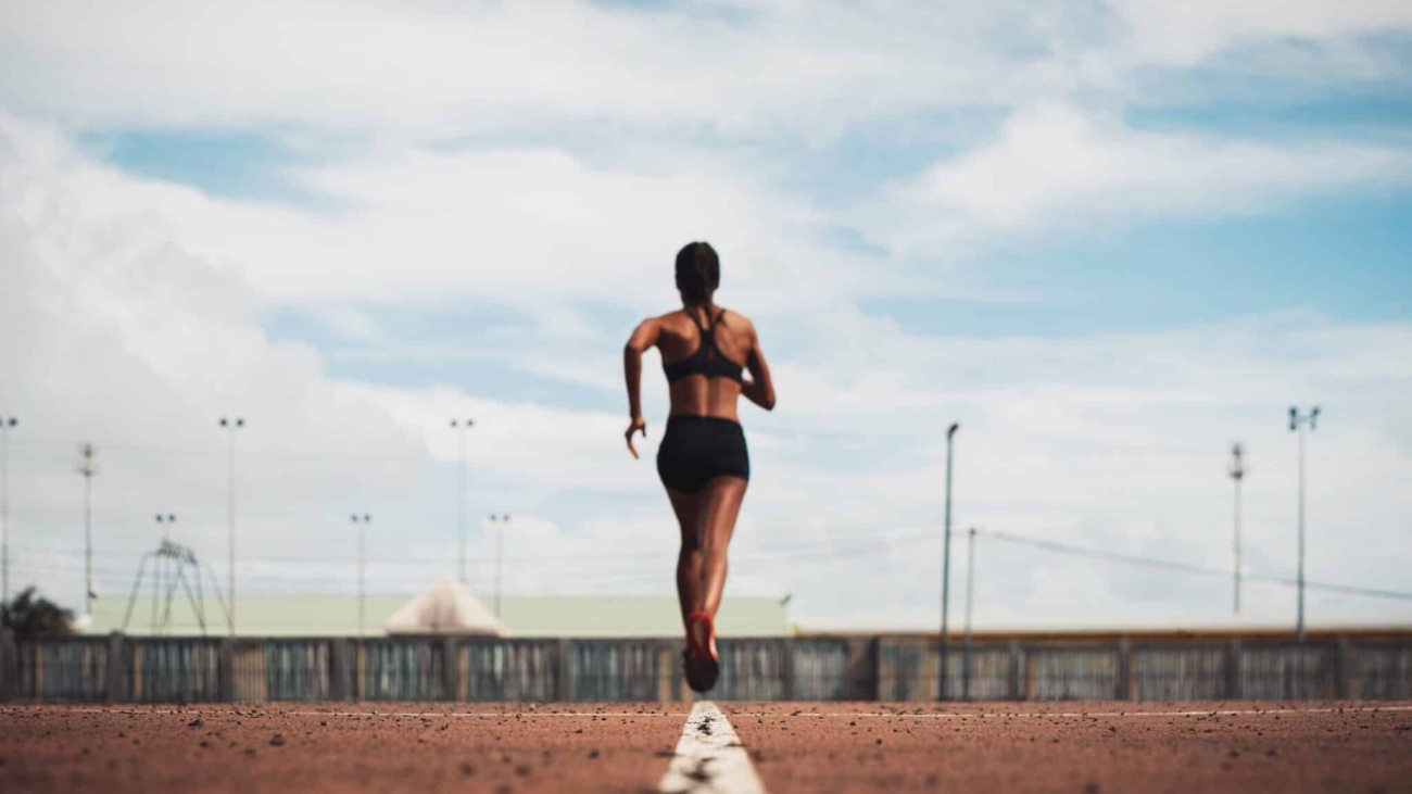 rear-view-female-athlete-running-track-field-against-sky