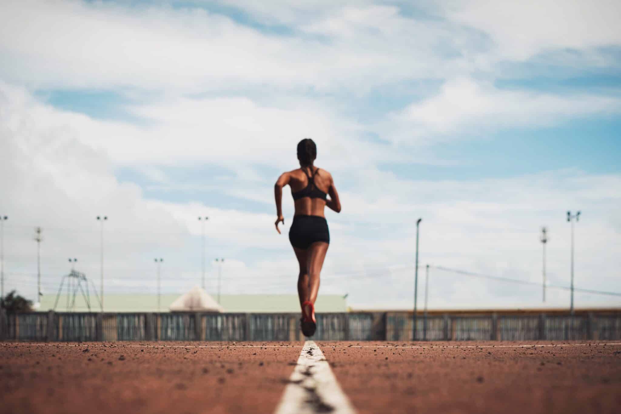 rear-view-female-athlete-running-track-field-against-sky
