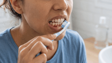 persona con encías que sangran al cepillarse los dientes frente al espejo